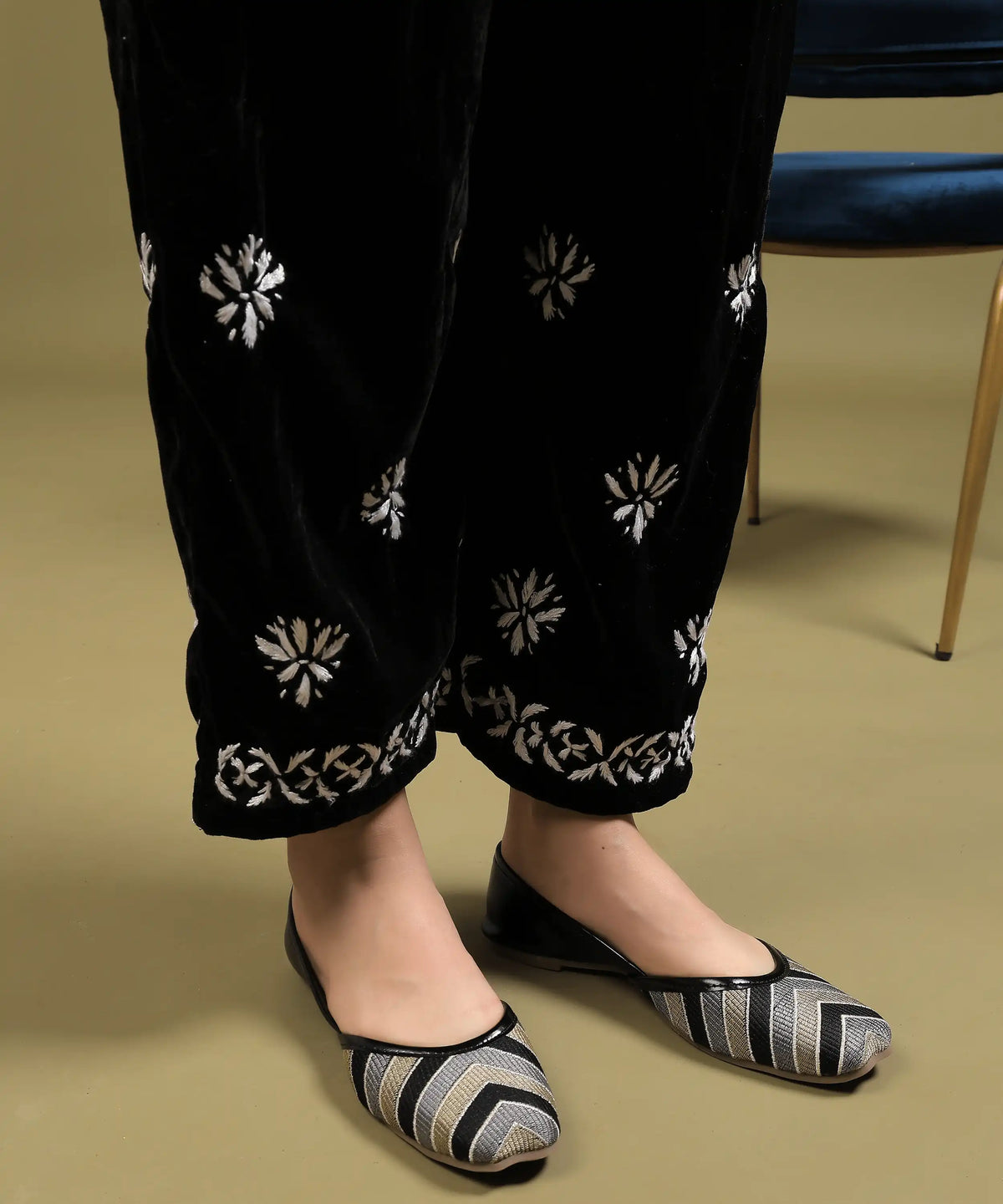 Close-up of white hand Chikankari embroidery on hem of black velvet pant from Ruh kurta set, beside blue chair — Noor-e-Awadh