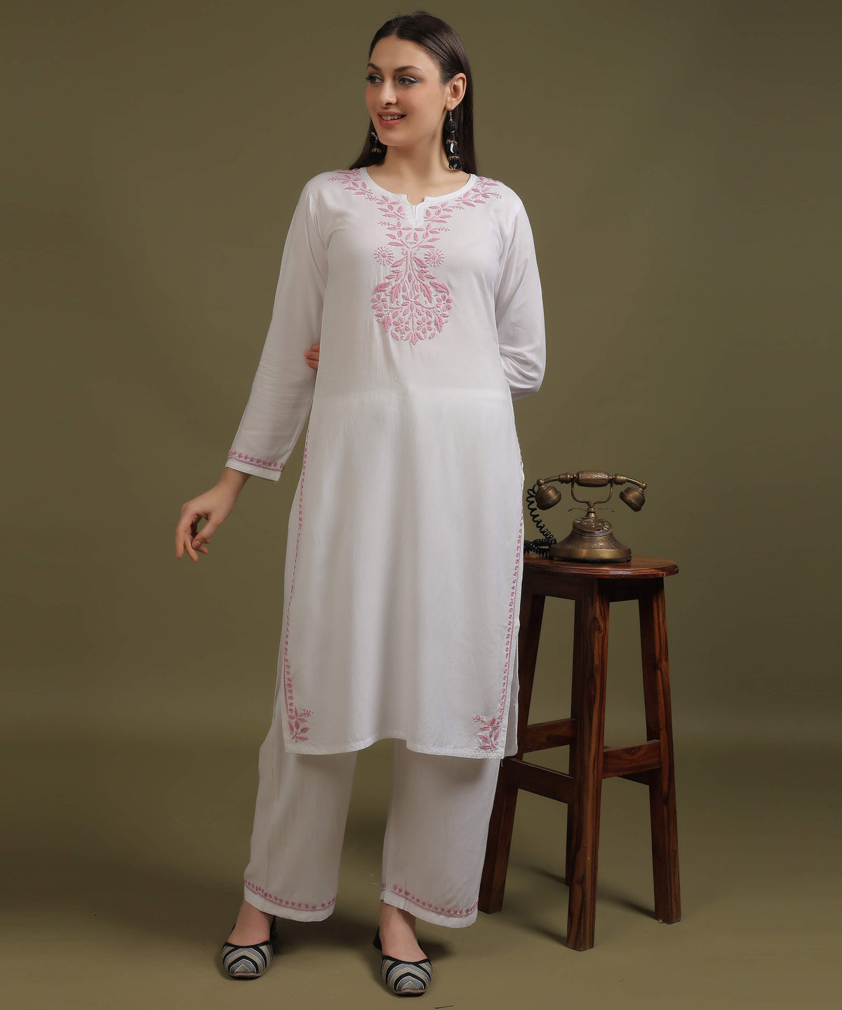 Model standing in NOORI white rayon chikankari palazzo set with pink Ghas Patti embroidery next to vintage telephone on wooden stool by Noor-e-Awadh